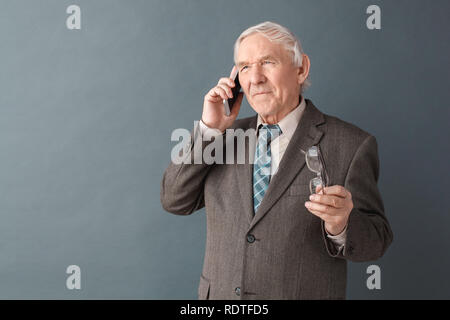 Älterer mann Studio stehen isoliert auf Grau holding Gläser annehmen Anruf zuhören besorgt Stockfoto