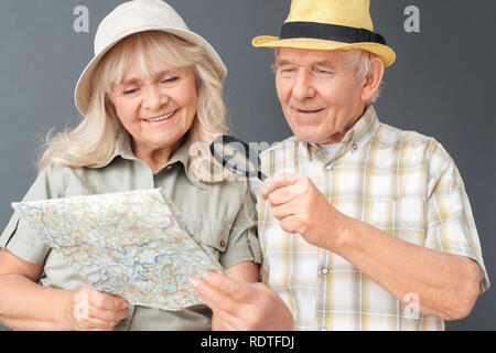 Ältere Touristen in Strand hüte Studio stehen auf Grau holding Lupe bei map glücklich close-up Stockfoto