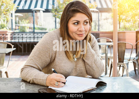 Ziemlich Hispanic Frau schreibt in einer Zeitschrift an einer im Cafe und lächelt in warmes Licht Stockfoto