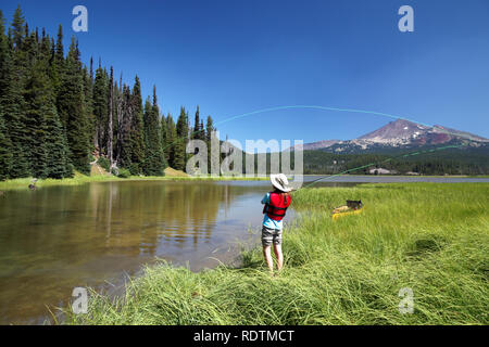 Mädchen Angeln vom Ufer entlang Kanal Funken See, gebrochene Spitze Berg im Hintergrund, Cascade Lakes, Oregon, USA Stockfoto