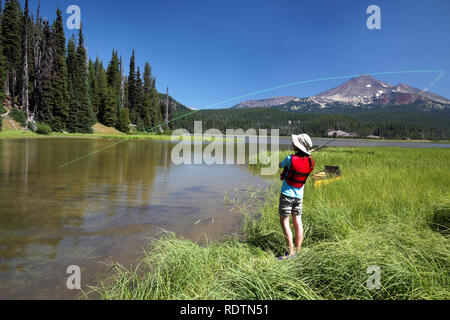 Mädchen Angeln vom Ufer entlang Kanal Funken See, gebrochene Spitze Berg im Hintergrund, Cascade Lakes, Oregon, USA Stockfoto