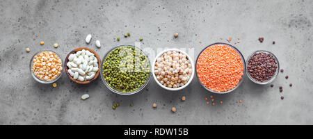 Sortiment bunte Hülsenfrüchte in Schalen, Linsen, Bohnen, Kichererbsen, mung, Erbsen auf konkreten Hintergrund, Ansicht von oben, Banner. Gesunde Ernährung, Diät Stockfoto