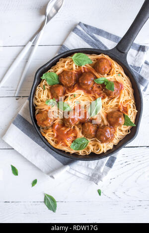 Spaghetti Nudeln mit Hackfleischbällchen, Tomatensauce und frischem Basilikum in gusseisernen Pfanne. Gesunde hausgemachten italienischen Teigwaren auf weißem Holz- Hintergrund mit Kopie spa Stockfoto