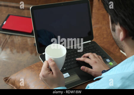 Der Mensch ist mit Laptop mit der Becher in der Hand. Stockfoto