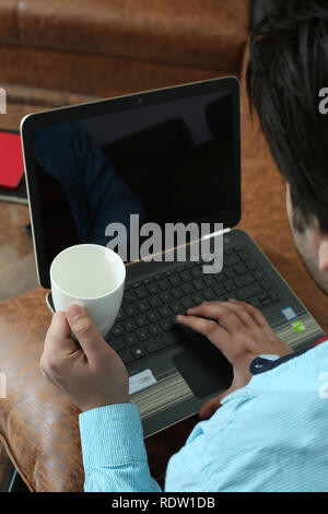 Mann arbeitet in Laptop und Holding mit der Kaffeetasse in der Hand. Stockfoto