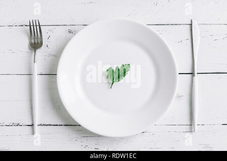 Tabelle Ambiente mit weißen Platte, modernes Besteck (Messer und Gabel) und kleine Blätter, frische Petersilie auf weißem Hintergrund, Ansicht von oben, kopieren. Diät, schnell Stockfoto
