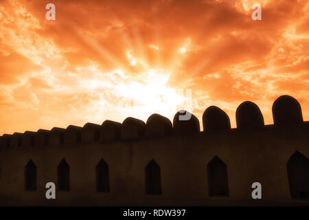 Nizwa fort Wände Silhouetten und Roter Himmel mit Strahlen, Durchbohren der Himmel Stockfoto