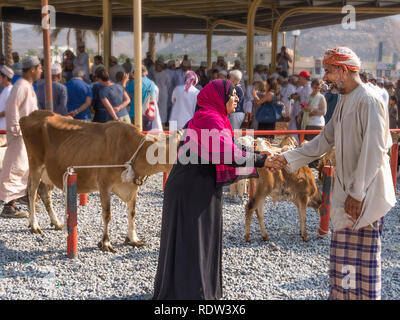 Nizwa, Oman - November 2, 2018: Frau mit Schleier und einem muslimischen Mann schütteln sich die Hände für die einkaufsvereinbarung am Freitag Tiermarkt in Nizwa Stockfoto