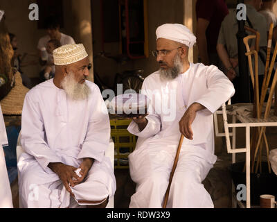 Nizwa, Oman - November 2, 2018: Omani mann Hände Halwa pack mit einem anderen Mann in traditioneller Kleidung am Nizwa Markt Stockfoto