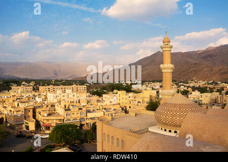 Nizwa, Oman - November 1, 2018: Detail der Minarett der Nizwa Moschee von oben und im Hintergrund die Häuser des Dorfes und der moun gesehen Stockfoto