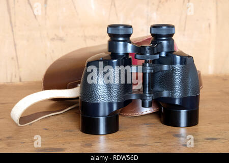 Vintage Englisch militärischen Prism schwarz Fernglas und öffnete Braun hart Ledertasche auf hölzernen Hintergrund Vorderansicht closeup Stockfoto