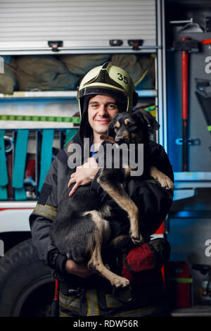 Foto von glückliche Feuerwehrmann in Helm mit Hund auf dem Hintergrund der fire truck Stockfoto