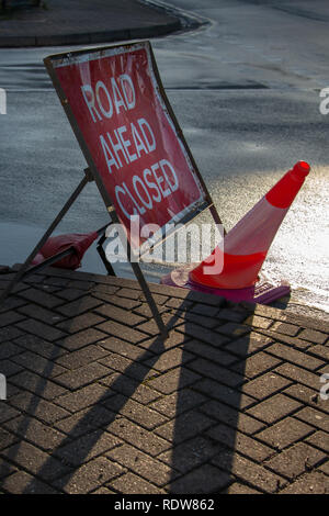 Straße geschlossen Schild mit zerquetschten Leitkegel und großen Regen Pfützen mit Reflexionen von Gebäuden nach Hochwasser Stockfoto