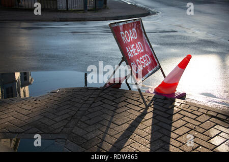 Straße geschlossen Schild mit zerquetschten Leitkegel und großen Regen Pfützen mit Reflexionen von Gebäuden nach Hochwasser Stockfoto