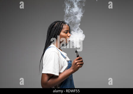 Junge afrikanische Frau mit und vaping eine elektronische Zigarette, E-Cig, ecigarette auf grauem Hintergrund Stockfoto