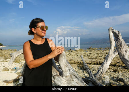 Junge Frau posiert auf dem Baum am Sandstrand Stockfoto