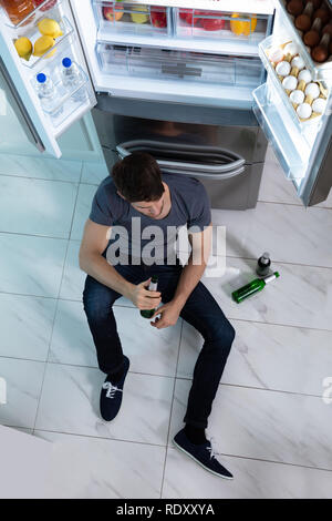 Hohe Betrachtungswinkel und der Mann sitzt in der Nähe der Kühlschrank in der Küche Bier trinken. Stockfoto