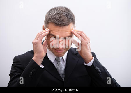Portrait von Reifen Geschäftsmann leidet unter Kopfschmerzen vor weißem Hintergrund Stockfoto