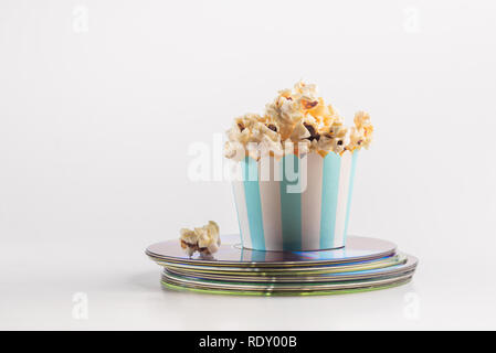 Miniatur-Eimer Popcorn auf einem Haufen Film-DVDs platziert. Ein Konzept für Home Entertainment. Verführerisches Popcorn im Papierbecher. Stockfoto