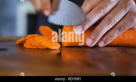 Hand schneiden Möhre auf Schneidebrett. Köche Händen zerkleinern Karotte auf Holzbrett Stockfoto