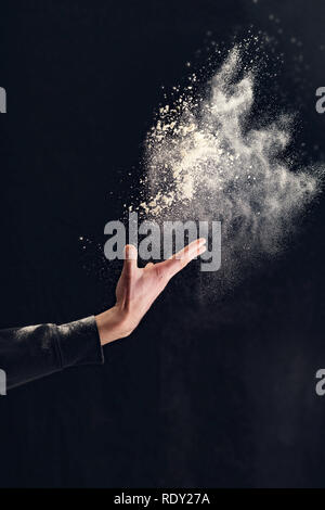 Die menschliche Hand halten Mehl auf schwarzem Hintergrund Stockfoto