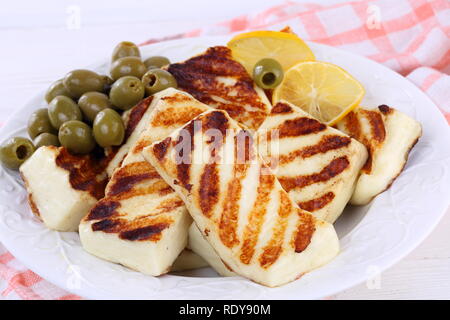 Gebratener Halloumi mit Zitronen und Oliven auf weissem Holztisch Stockfoto