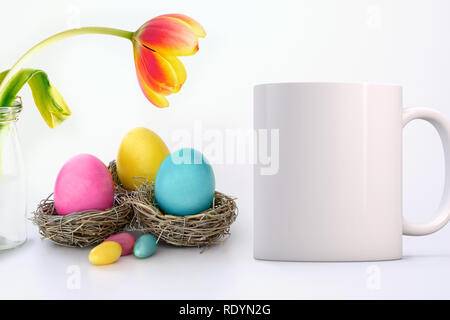 Weiße leere Tasse weiter zu farbigen Eier in Nester und eine hübsche Tulpe. Perfekt für Unternehmen Tassen verkaufen, nur Overlay ihr Angebot oder Design auf t Stockfoto