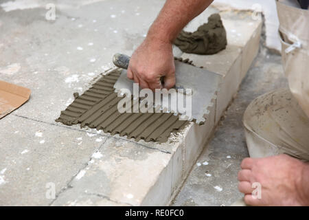 Die Bauarbeiter breitet sich gleichmäßig die Oberfläche der Treppe mit Zement Klebstoff mit einem speziellen Werkzeug Hand Masse. Stockfoto