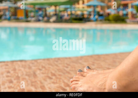 Natürliche Beleuchtung und Schatten von den Beinen des blur Frau am Tag Bett neben Pool im Resort. Sonnenbaden und Chillen am Pool im Sommer Konzept Stockfoto