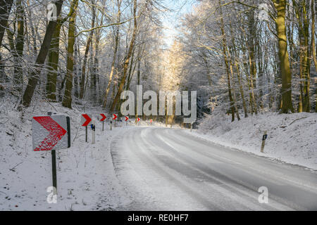 Verkehrszeichen mit roten Pfeilen auf eine gefährliche Kurve auf einer verschneiten Landstraße durch den Winterwald, Sicherheit fahren Konzept, kopieren Raum Stockfoto