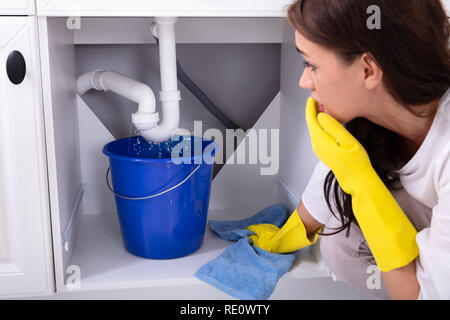 Nahaufnahme einer jungen Frau die blauen Eimer unter Wasser leckt von der Spüle Leitung Stockfoto