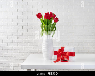 Rote Tulpen in weiße Vase neben einer Geschenkbox mit roter Schleife Stockfoto