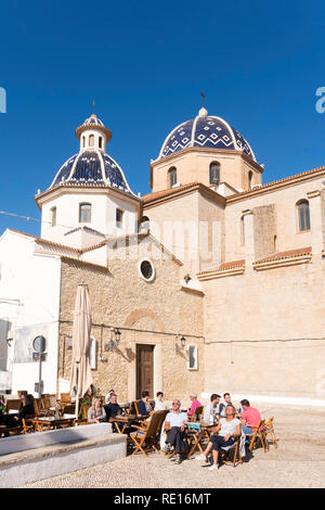 Die Menschen sitzen draußen in einem Café vor der Kirche von La Mare de Déu del Consol in Altea, Costa Blanca, Spanien, Europa Stockfoto