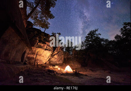 Fantastische Landschaft am Sommer, der Nacht. Hell brennen kleine Lagerfeuer im Canyon inmitten von riesigen steilen Felsen unter klaren dunklen Sternenhimmel. Tourismus, Sicherheit, Klettern, Wandern und Reisen. Stockfoto