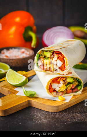 Gegrillte burritos Wraps mit Hühnerfleisch, Bohnen, Mais, Tomaten und Avocado auf einem Holzbrett, dunklen Hintergrund. Fleisch burrito, mexikanisches Essen. Stockfoto