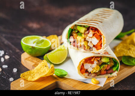 Gegrillte burritos Wraps mit Hühnerfleisch, Bohnen, Mais, Tomaten und Avocado auf einem Holzbrett, dunklen Hintergrund. Fleisch burrito, mexikanisches Essen. Stockfoto