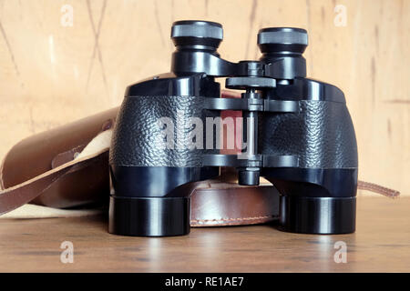 Vintage Englisch militärischen Prism schwarz Fernglas und öffnete Braun hart Ledertasche auf hölzernen Hintergrund Vorderansicht closeup Stockfoto