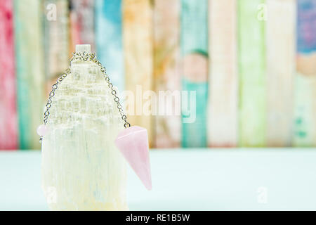 Mit crystal Selenit Turm für das Laden von rosenquarz Pendel, hellblau Tabelle und pastellfarbenen Holzbrett Hintergrund. Divination, Wahrsagen Stockfoto