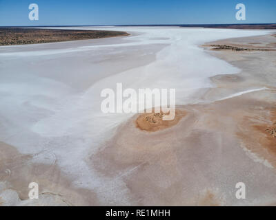 Aus der Vogelperspektive auf ein riesiges salziges Gelände mit weißen Salzebenen, umgeben von trockenem Land unter einem klaren blauen Himmel Stockfoto