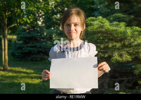 Süße kleine Schulmädchen mit leeren Blatt Papier für Werbung auf Natur Hintergrund. Stockfoto