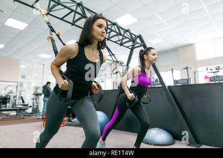 Gruppentraining mit Fitness Schleifen in der Turnhalle, zwei junge attraktive Athlet Frauen tun crossfit mit Gurten. Sport, Teamarbeit, Training, Personal Stockfoto