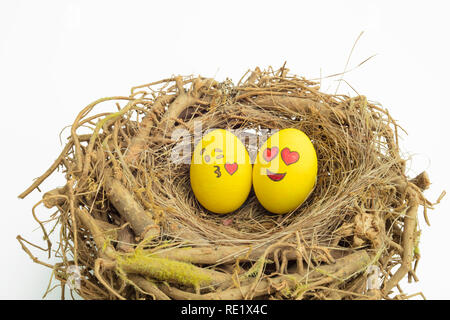 Zwei Ostereier bemalt mit Emojis, eins in der Liebe und anderen küssen, in isolierten weißen Hintergrund in ein Nest gelegt. Stockfoto