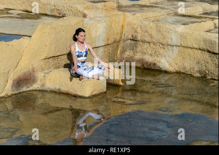 Frau, meditieren, das Üben der 'Easy pose' unter den Kalkstein Salinen in Malta Stockfoto
