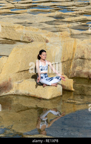 Frau, meditieren, das Üben der 'Easy pose' unter den Kalkstein Salinen in Malta Stockfoto