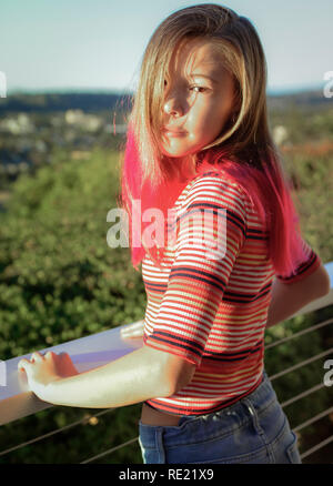 Tween girl mit trendigen Dip dyed rosa Haaren und mit ihr die Augen aus emotionlessly außerhalb starrte auf dem Balkon Stockfoto