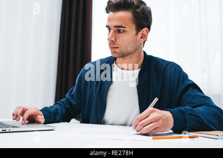Konzentriert man schreiben neue Ideen in Notepad Suche auf dem Bildschirm Laptop. Junge Mitarbeiter sitzt am Tisch und die Arbeit im Büro Stockfoto