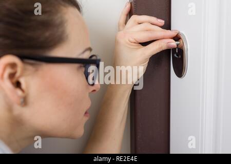 Frau lugen im Schlüsselloch, zu Hause in der vorderen Tür. Stockfoto