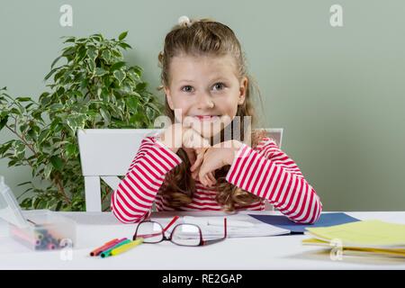 Niedlich junior Schülerin mit blonden Haaren, lächelnd, Zeichnung in einer Schule Notebook und Spaß zu Hause an einem Tisch Stockfoto