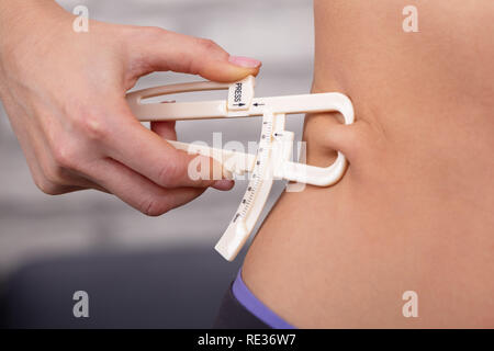 Nahaufnahme von einer Frau, die Hand mit einer Schieblehre messen Körperfett auf Taille Stockfoto