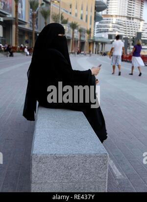 Arabische Frau in der traditionellen schwarzen Kleid, die Abaya, mit Handy, Dubai Mall, Dubai, Vereinigte Arabische Emirate, Naher Osten Stockfoto